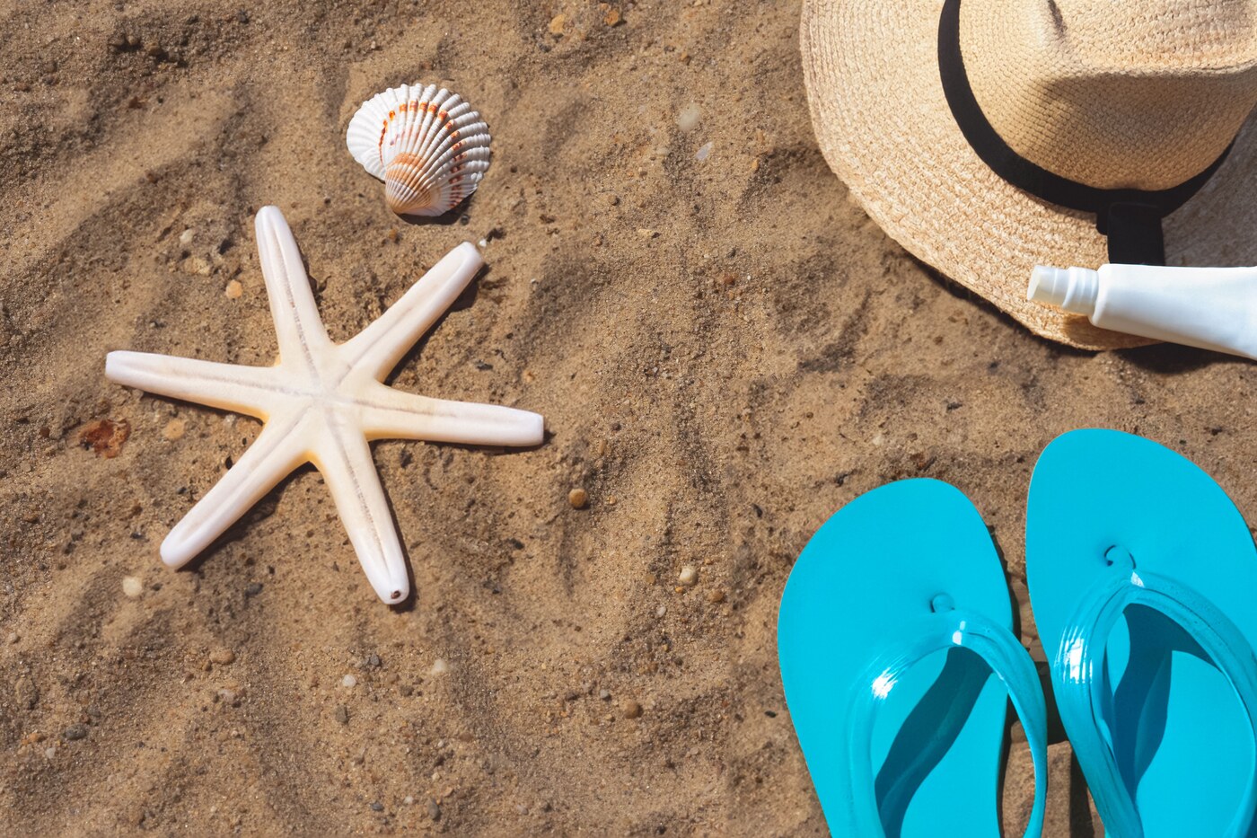 Chapeau, lunettes et produits solaires disposés sur le sable
